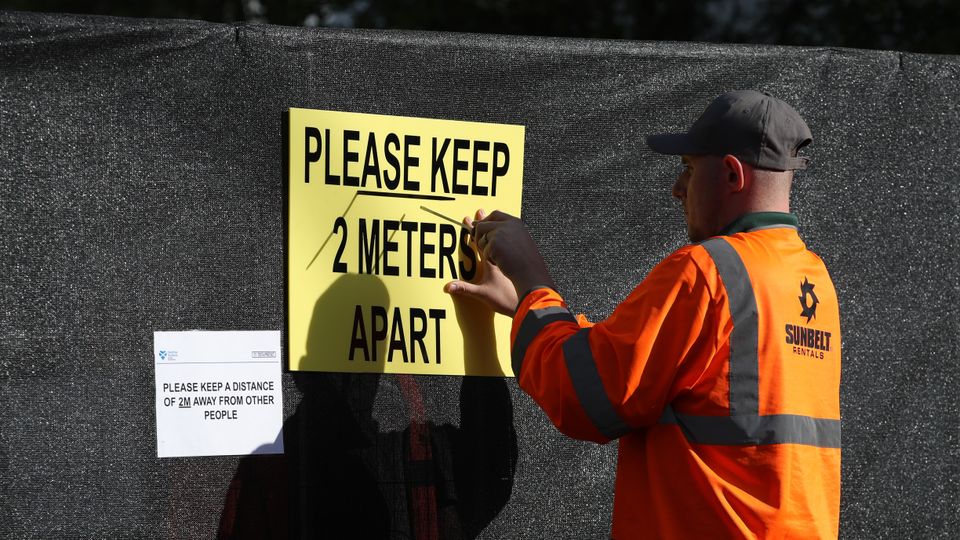 Worker puts up please keep two metres apart sign