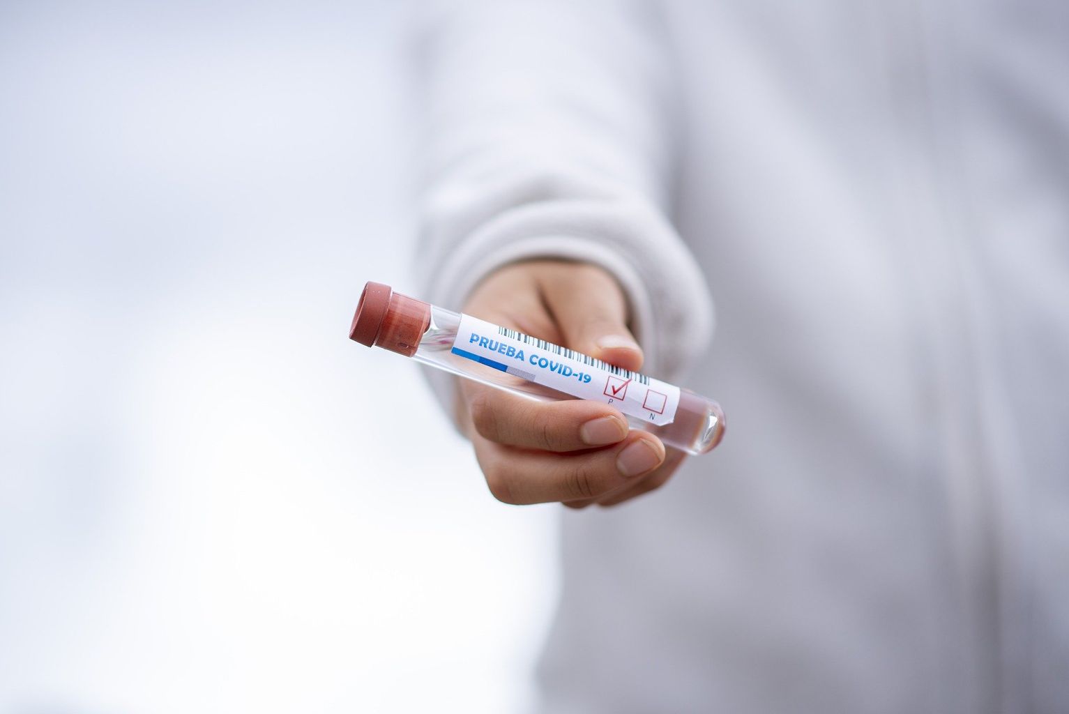 person holding a sealed test tube with a label saying covid on it