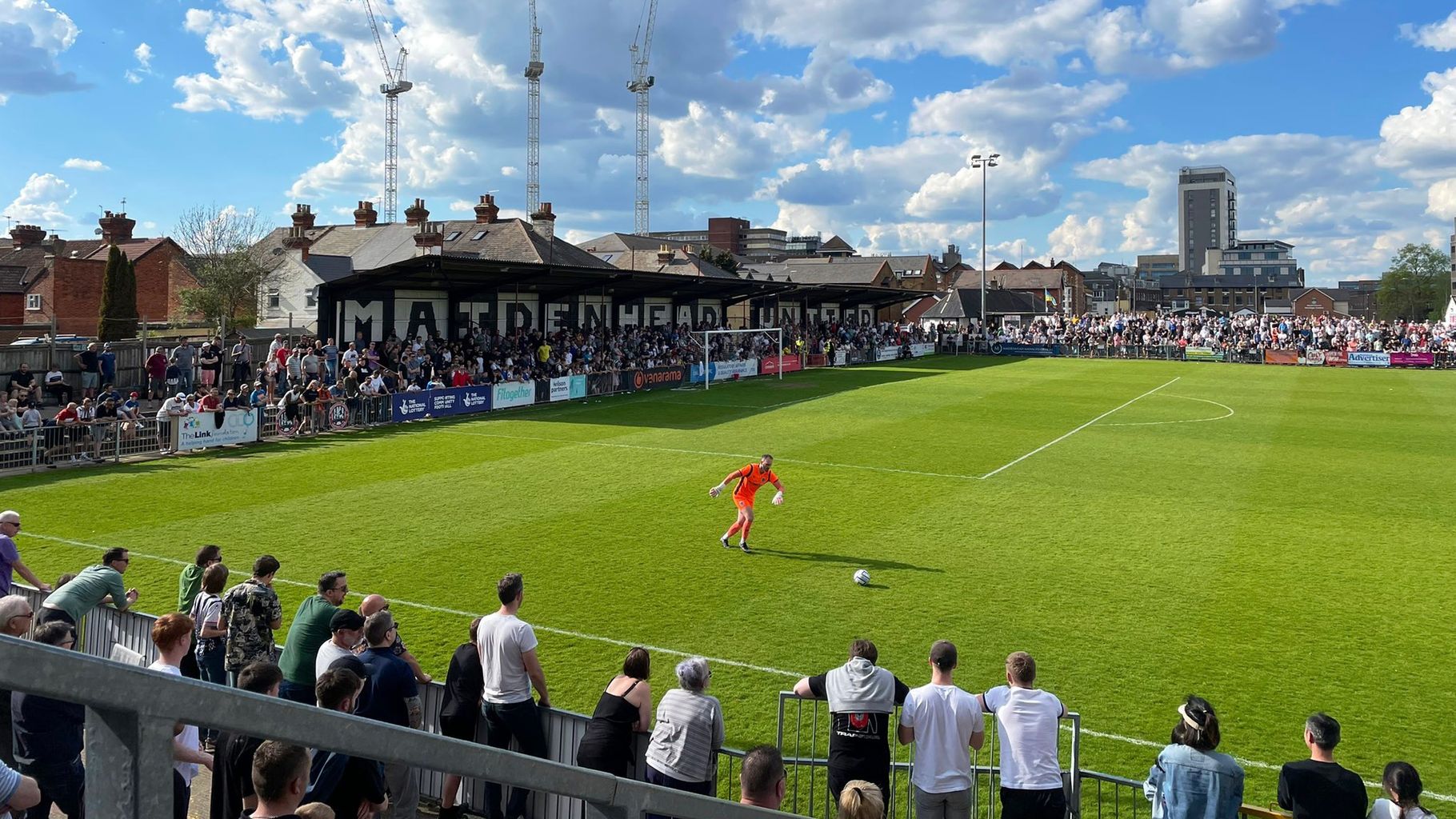  A football match is taking place at York Road stadium, home of Maidenhead United football club, with a large crowd of spectators looking on.