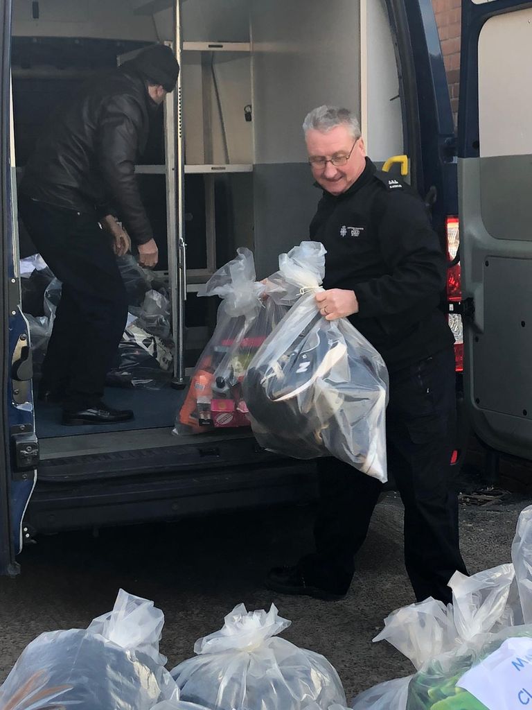 Police officers loads bags of goods onto the back of a van.