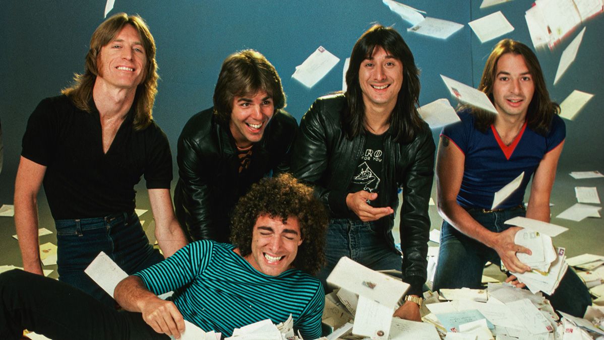 The rock band Journey poses together surrounded by piles of fan mail in a playful promotional photo from the 1980s, featuring lead singer Steve Perry.