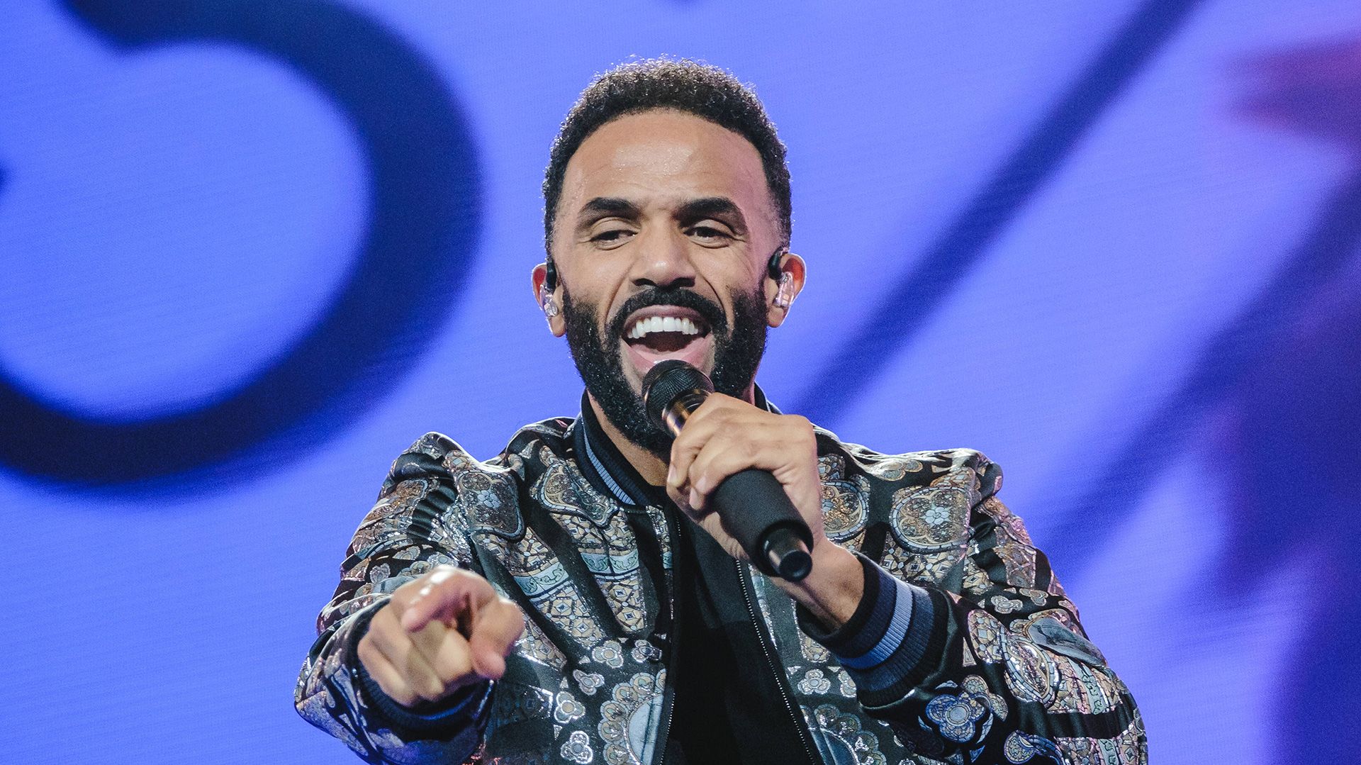 Craig David performing on stage, singing into a microphone.